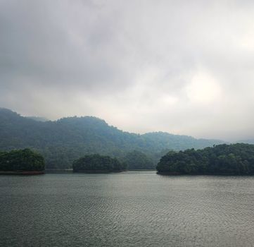 Serene view of Periyar Lake in Kerala, India with misty hills and dense greenery under cloudy skies.