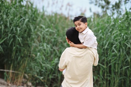 Free A father carrying his cheerful child on a sunny day in Salyan, surrounded by lush green plants. Stock Photo