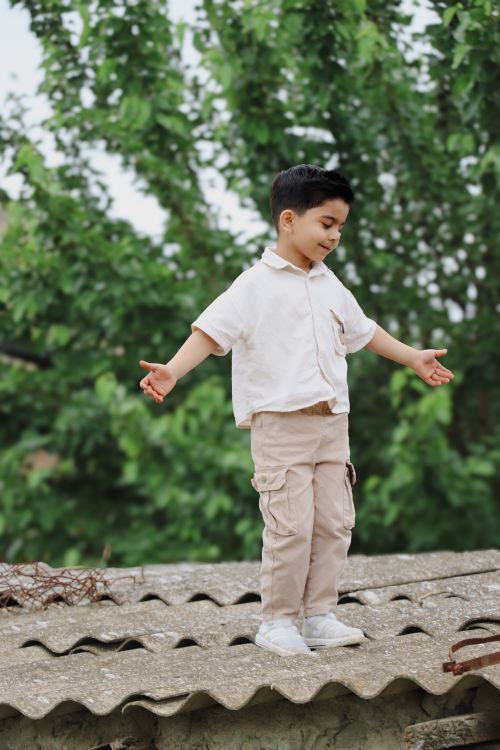 Free A young boy joyfully plays on a rooftop against a backdrop of lush greenery in Salyan, Azerbaijan. Stock Photo