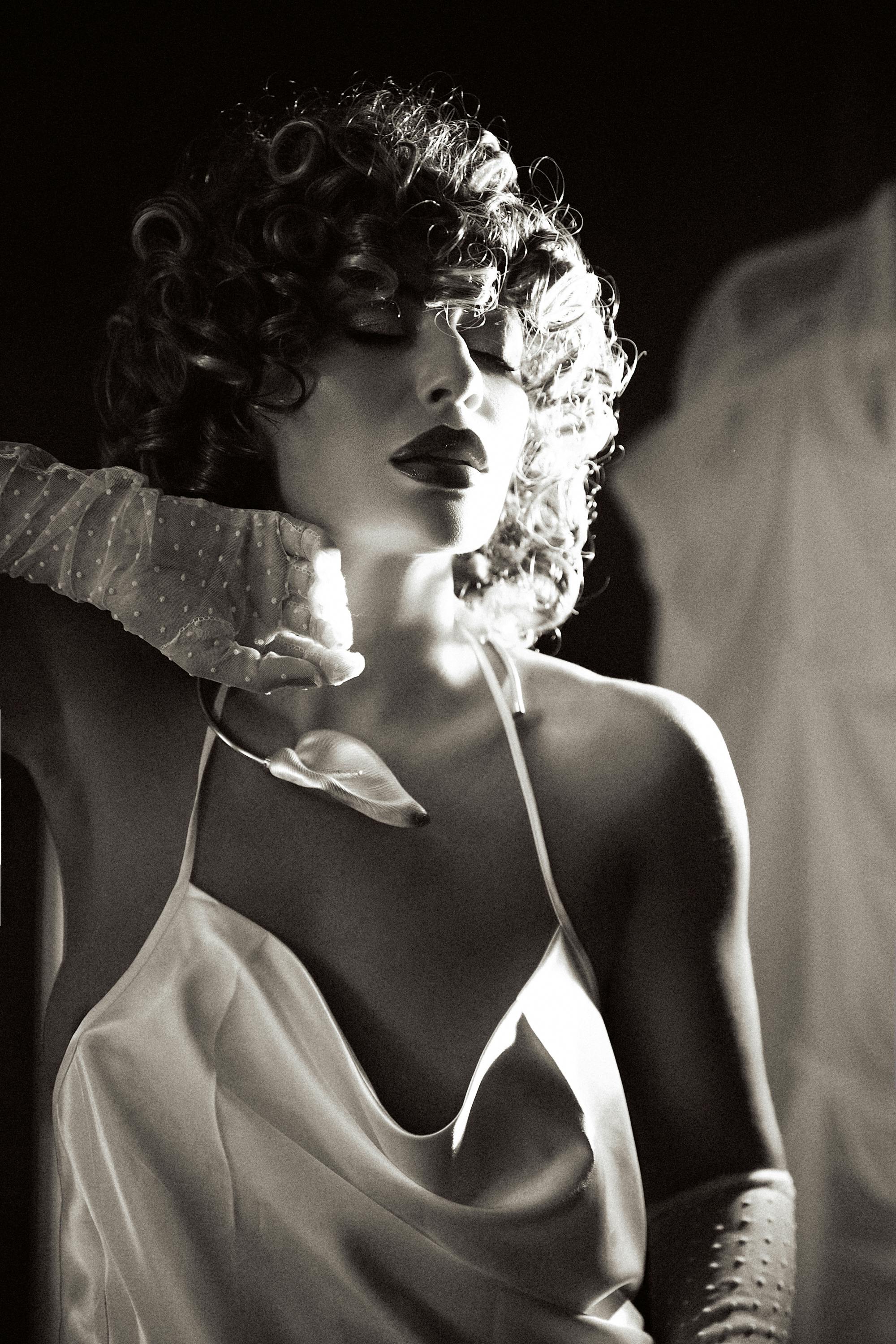 Elegant black and white portrait of a woman with curly hair and gloves.
