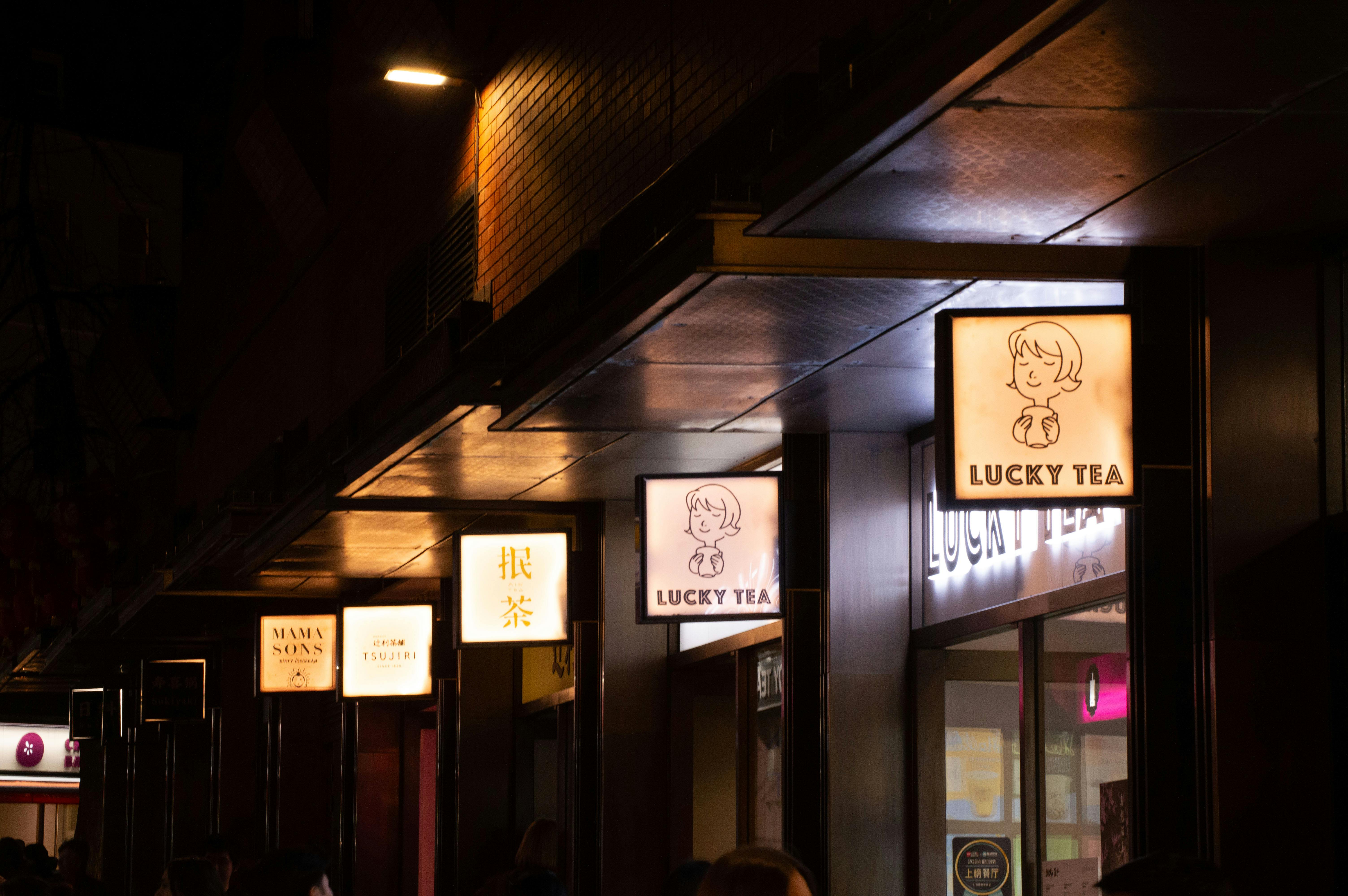 Free Nighttime urban scene in Chinatown featuring glowing tea shop signs on a dark street. Stock Photo