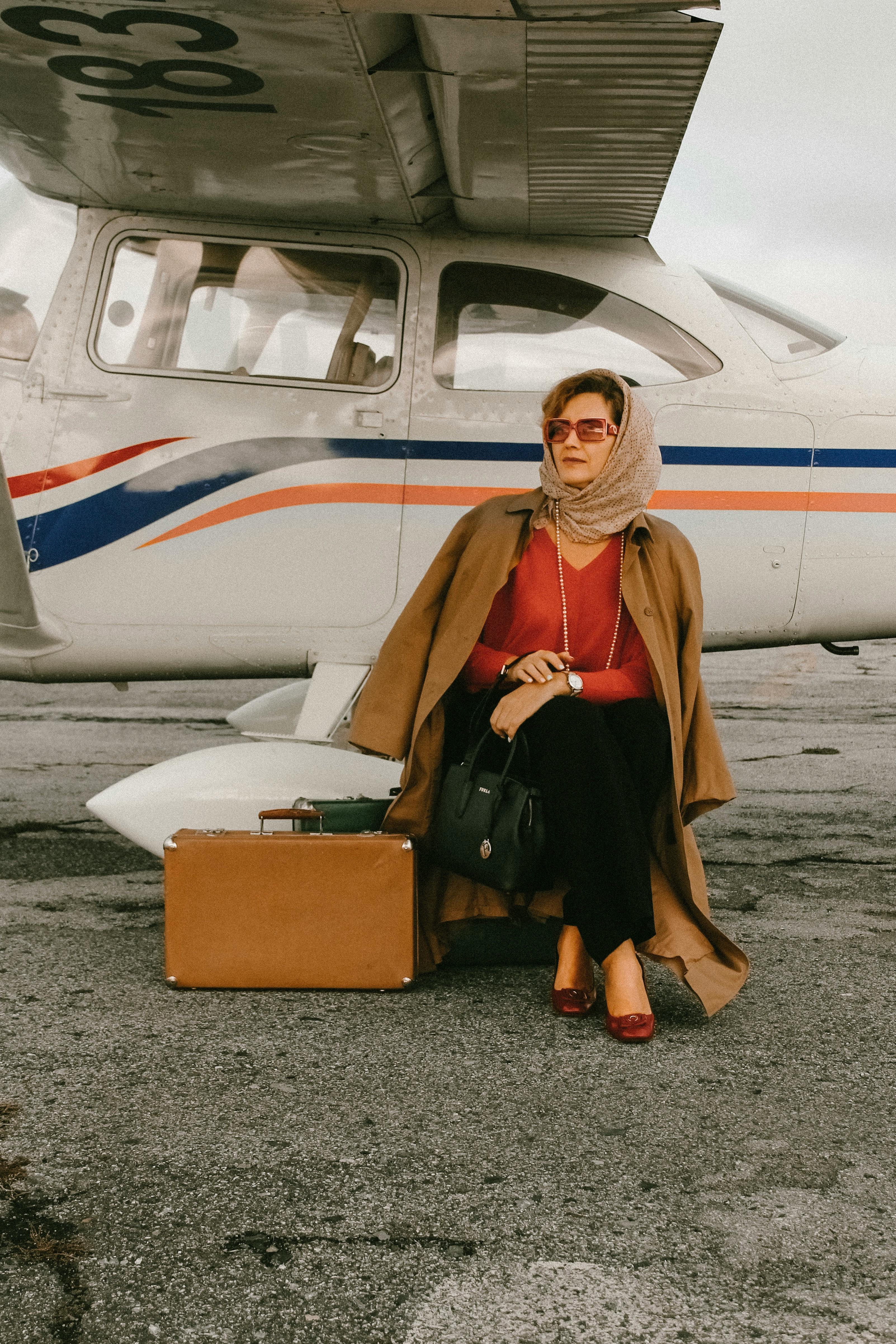 一位穿着时尚的优雅女士提着行李，坐在老式飞机旁，准备旅行