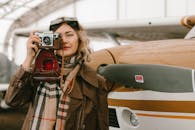 一位时尚女性在开放机库的飞机旁拿着老式相机摆姿势