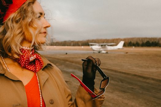 A fashionable woman with a red scarf and sunglasses standing near a small airplane.