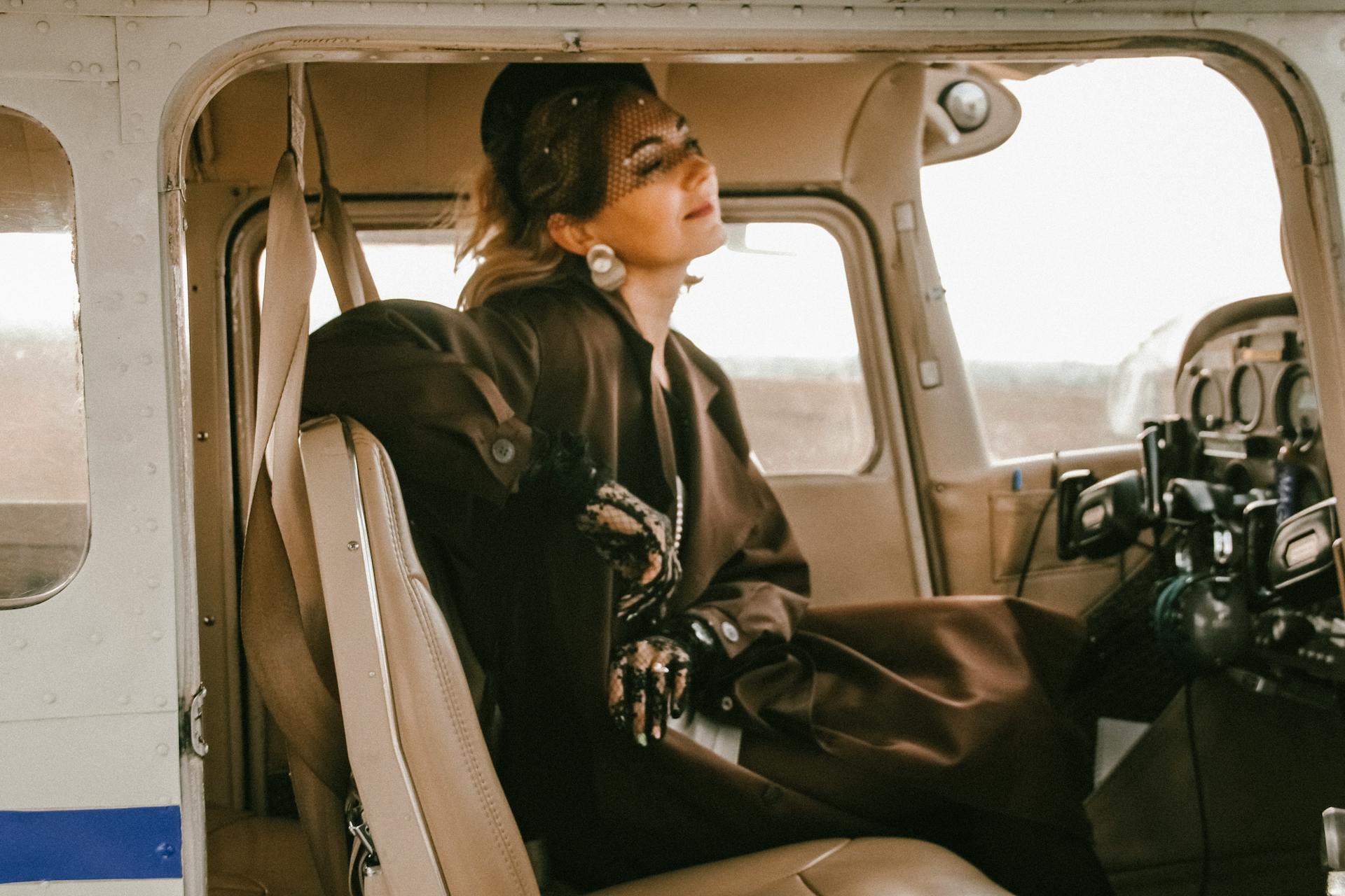 A stylish woman in vintage attire relaxes inside a private airplane cabin during daylight.