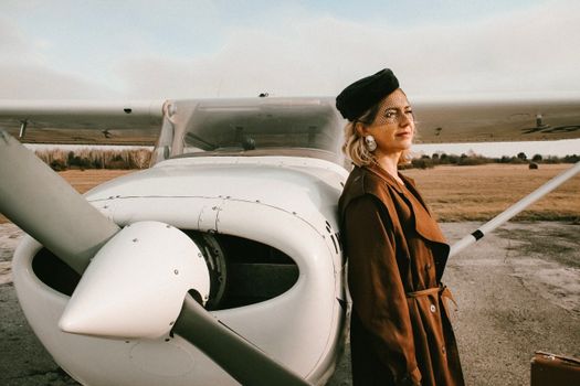 Elegant woman with blond hair standing by small aircraft in daylight