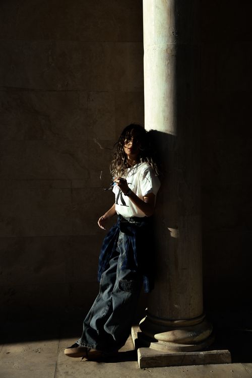 Free Stylish woman leaning against a column in dramatic light and shadow play. Stock Photo