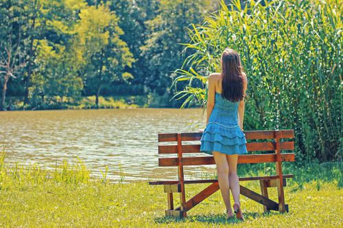 Free Woman enjoying a peaceful moment by a lake, embracing nature in summer. Stock Photo