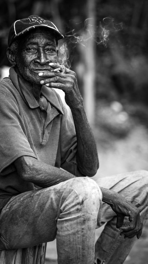 Free Black and white portrait of a senior Jamaican farmer enjoying a cigarette outdoors. Stock Photo