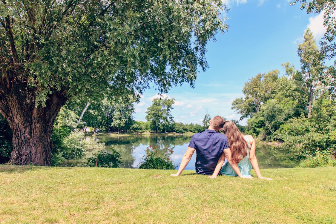 Free Couple Sitting on Grass Field in Front of Body of Water Stock Photo