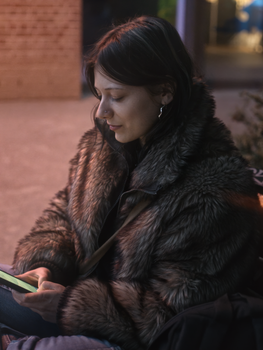 A young woman in a fur coat using her phone at night outdoors.