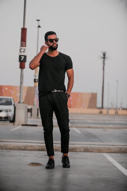 Fashionable man in all-black outfit posing confidently in an urban outdoor setting.