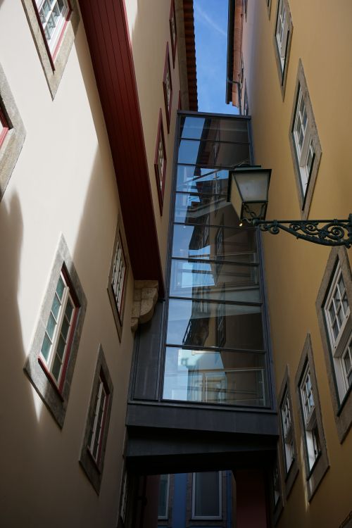 Free A narrow urban alleyway in Porto with modern glass bridge connecting historic buildings. Stock Photo
