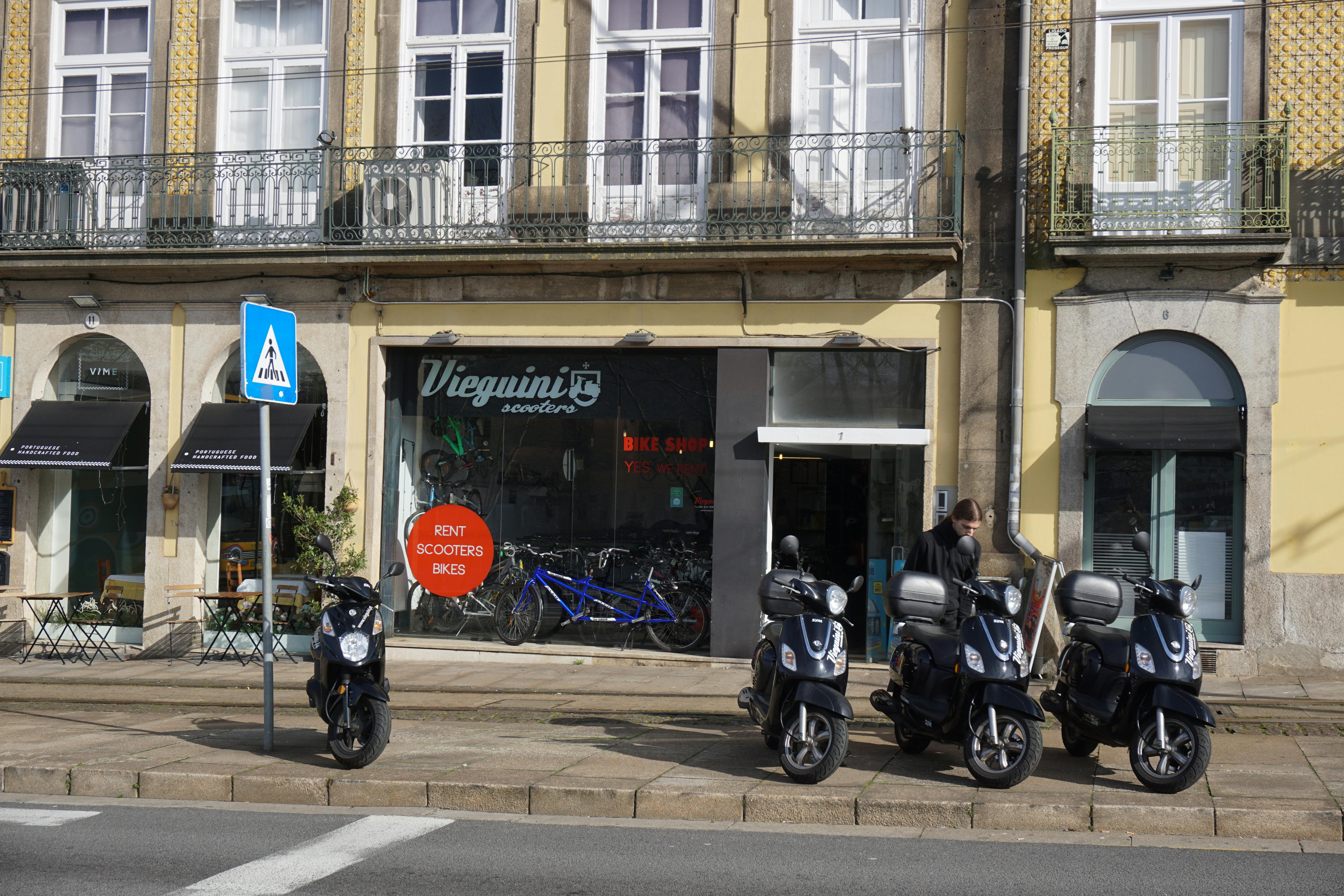 Vieguinis Scooters rental shop exterior in Porto with parked mopeds and bicycles.