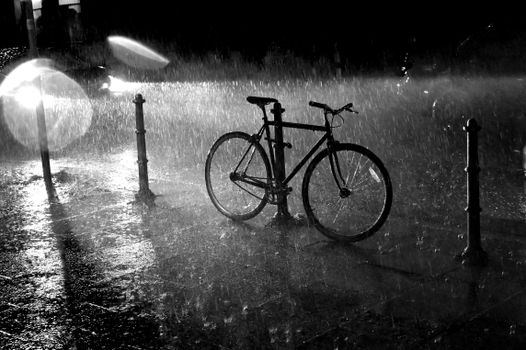 A solitary bicycle parked in the rain on an urban street at night, illuminated by streetlights.
