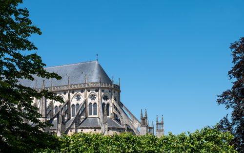 Free Stunning Gothic cathedral with lush greenery and bright blue sky, evoking historical elegance and tranquility. Stock Photo