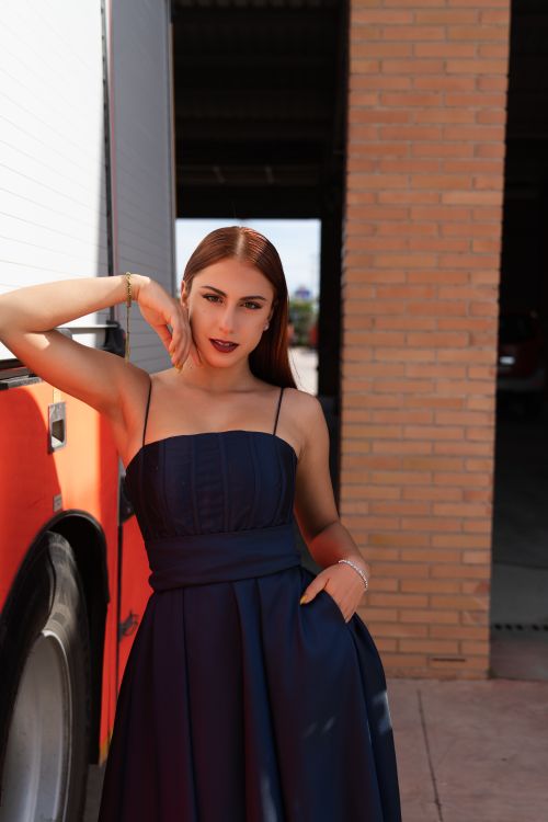 Free Stylish woman in blue dress posing against a red brick wall with natural lighting. Stock Photo