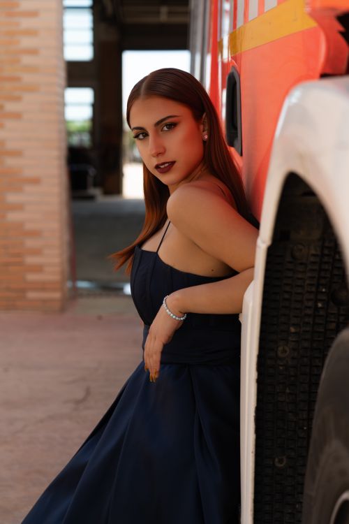 Free Stylish woman in formal dress leaning against a fire truck, showcasing elegance and strength. Stock Photo