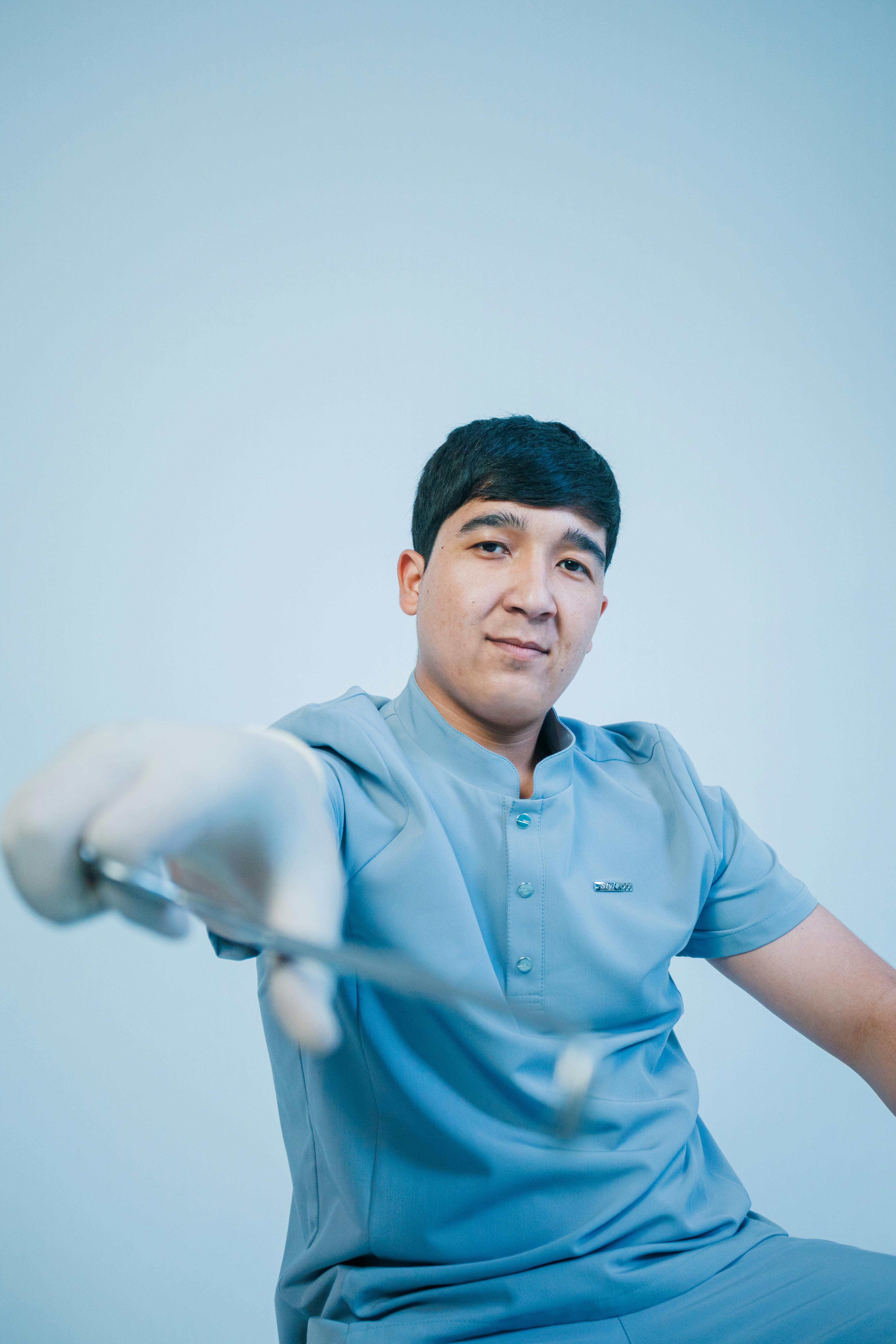 A confident young dentist in blue scrubs examining a dental instrument.