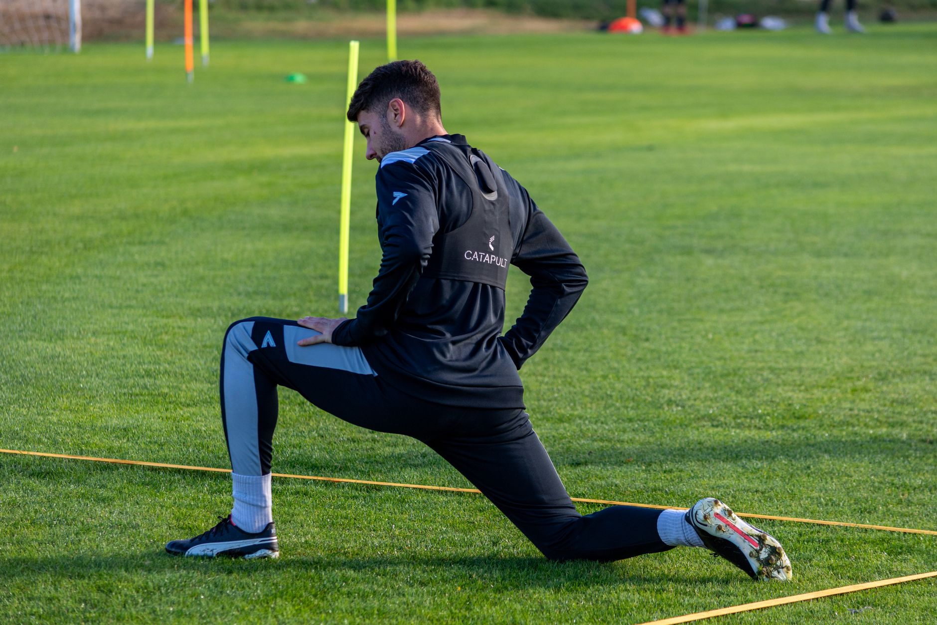 A young footballer training alone on a wet outdoor pitch, cones arranged precisely under stadium lights