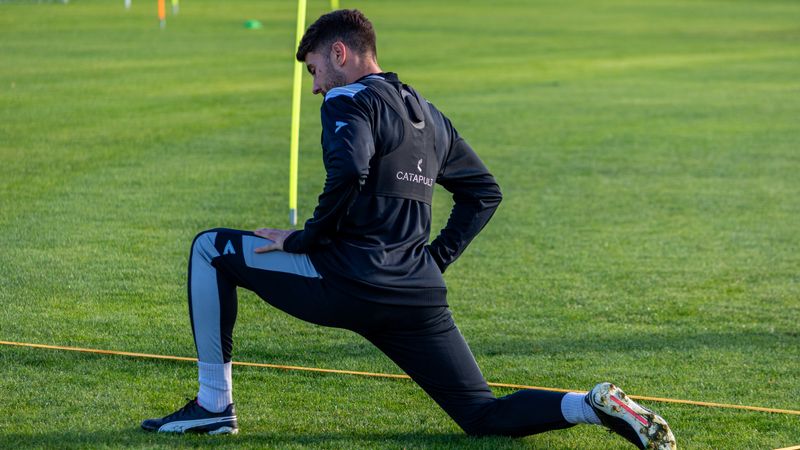 Football player stretching during outdoor training on a sunny day.