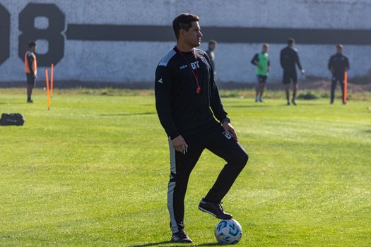 Adult soccer coach guiding players during outdoor training on a sunny day.