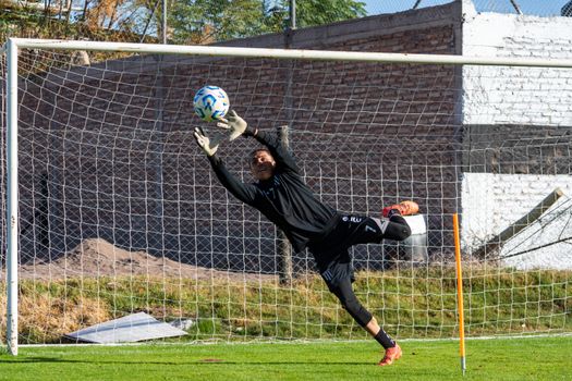 A focused soccer goalkeeper making an impressive save during a game on a sunny day.