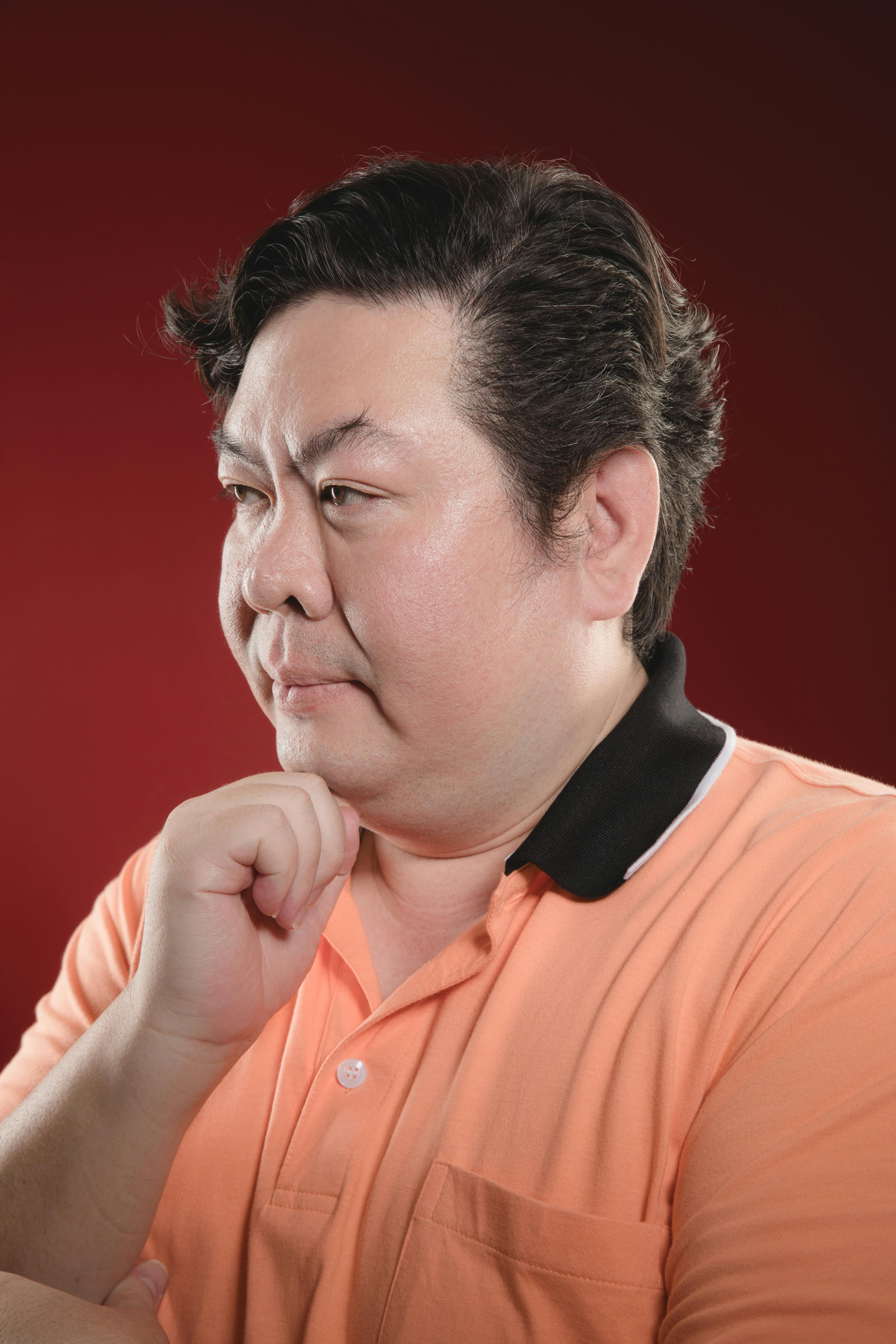 Безкоштовне Чоловік у помаранчевій сорочці задумливо позує на червоному тлі. стокове фото