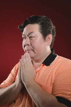 A serene portrait of a man with hands in prayer against a deep red backdrop, conveying peace and meditation.