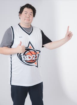 Man posing confidently in a BD27 basketball jersey, indoors with positive gesture.