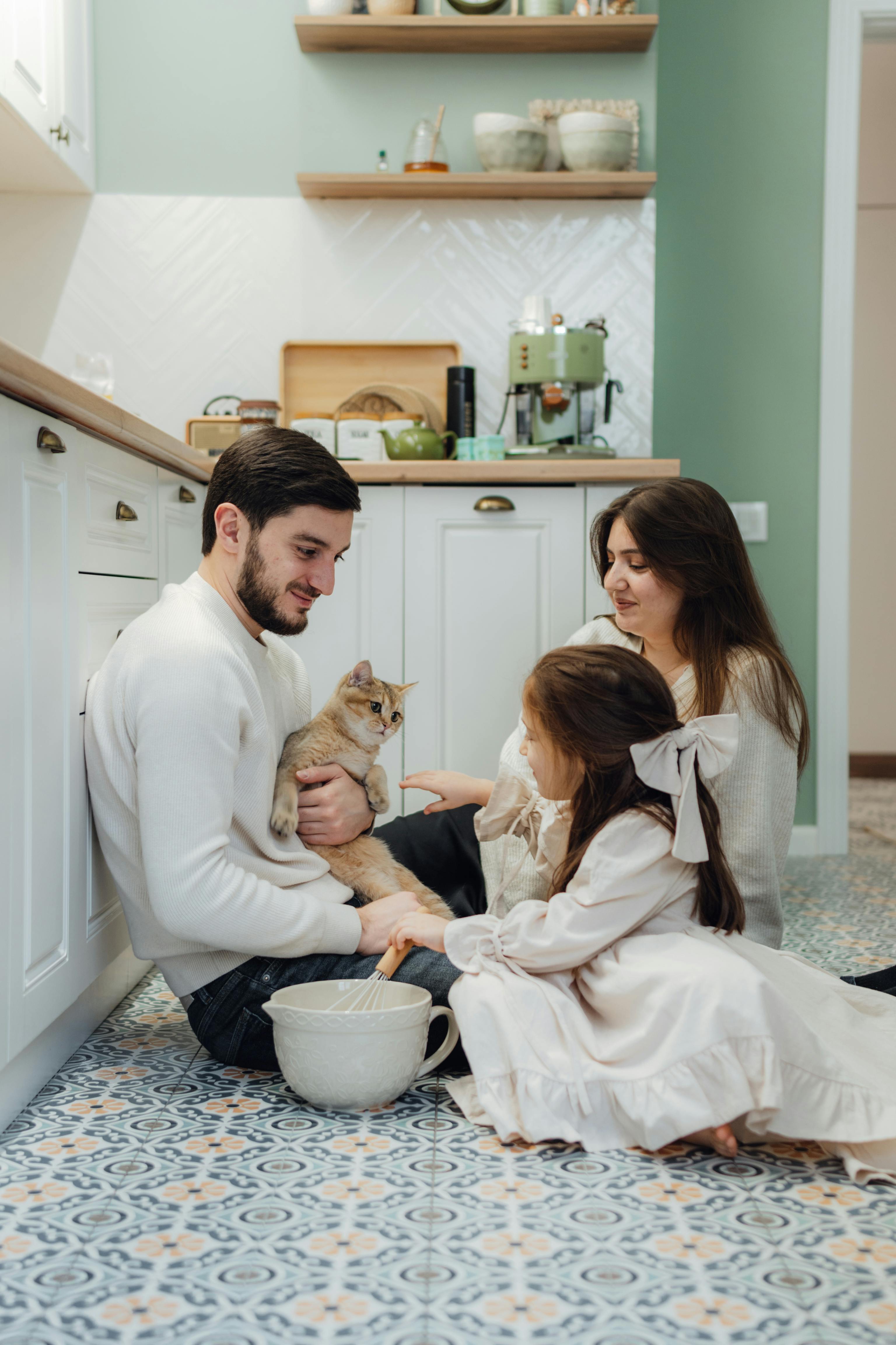 A family spends a warm moment with their cat in a bright, modern kitchen setting.
