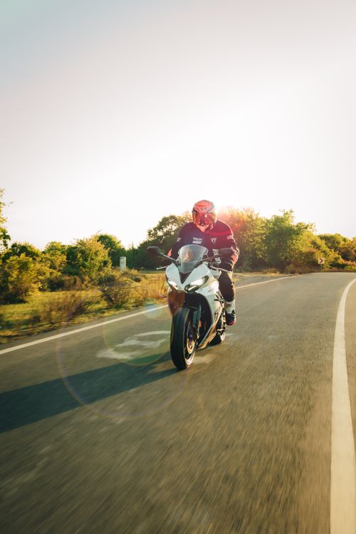 Free A motorcyclist rides a sports bike on an open road during sunset, surrounded by nature. Stock Photo