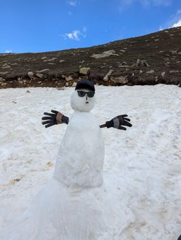 A stylish snowman wearing sunglasses and gloves stands on a rocky snow-covered hill.