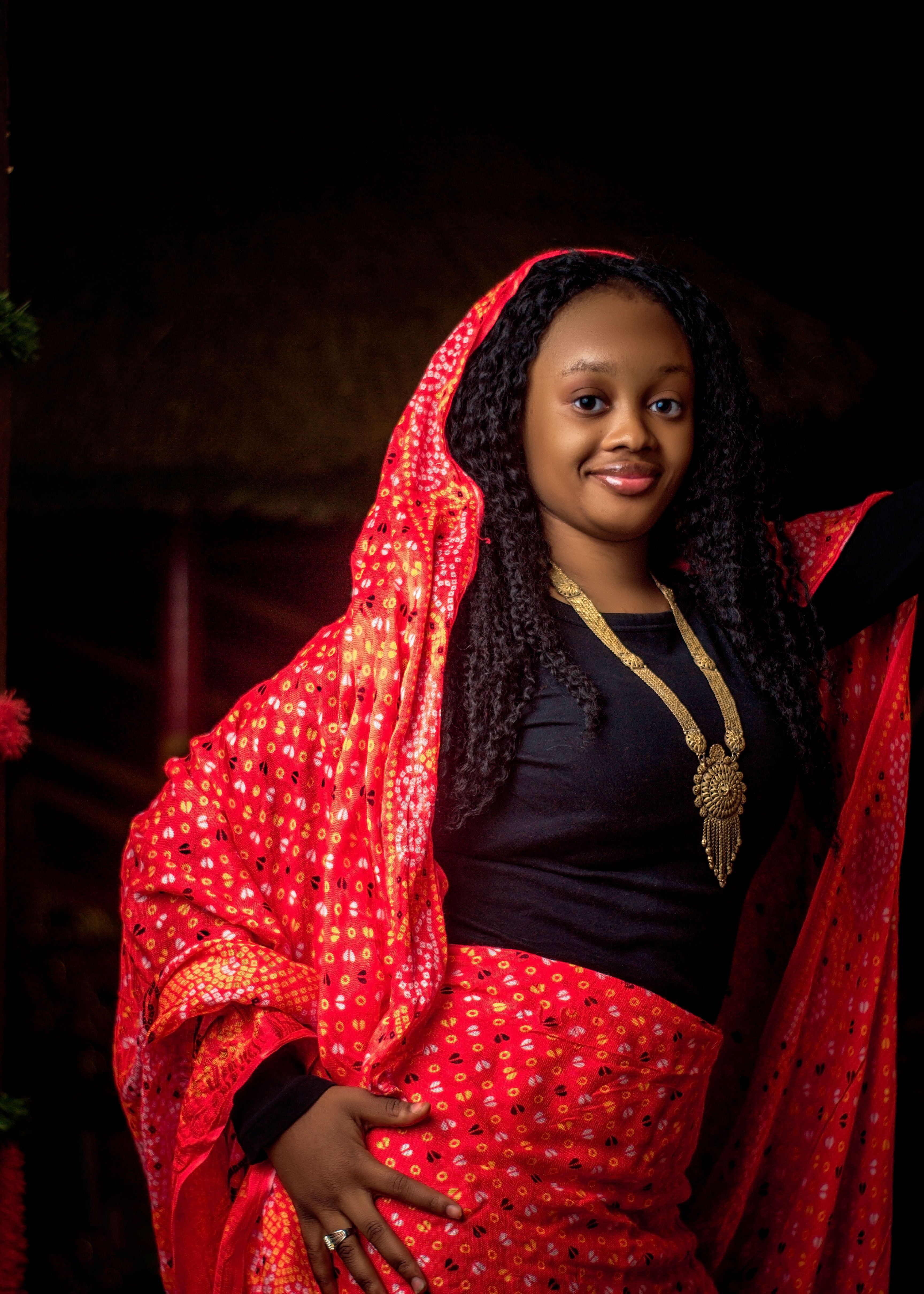 Portrait of a smiling woman in traditional red attire with gold jewelry.