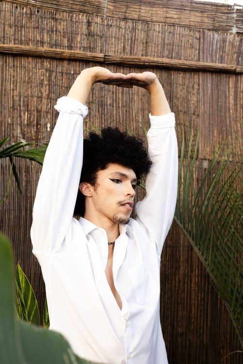 Free Male portrait featuring a stylish man in a white shirt, set against a natural backdrop with bamboo and plants. Stock Photo