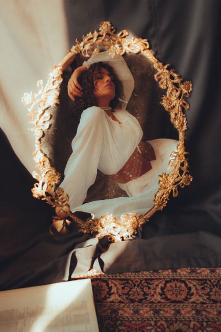 A woman in vintage attire reflected in an ornate gold mirror, creating an artistic, dreamy composition.
