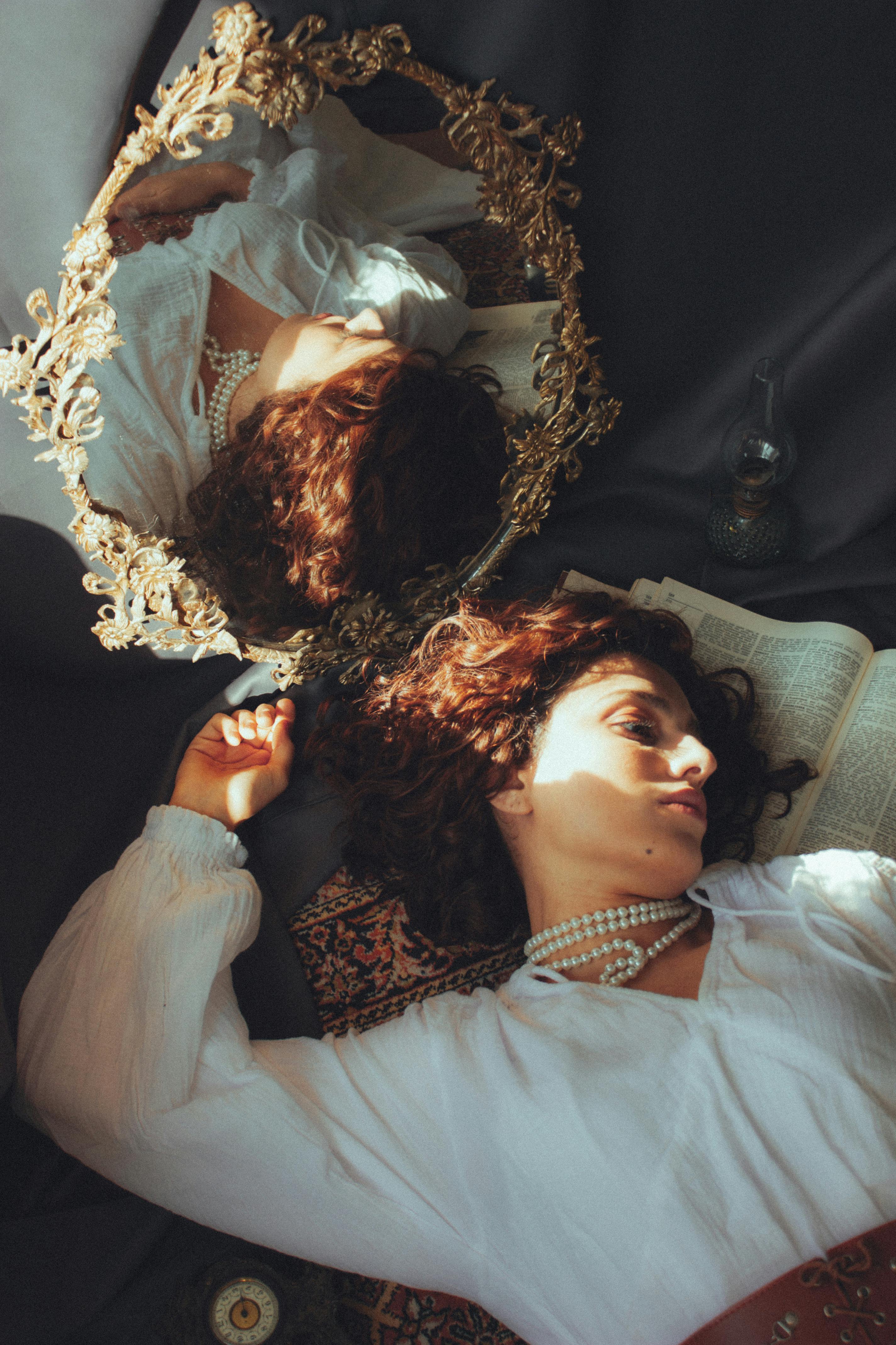 Woman in vintage attire lying beside ornate mirror. Reflective and artistic setting.