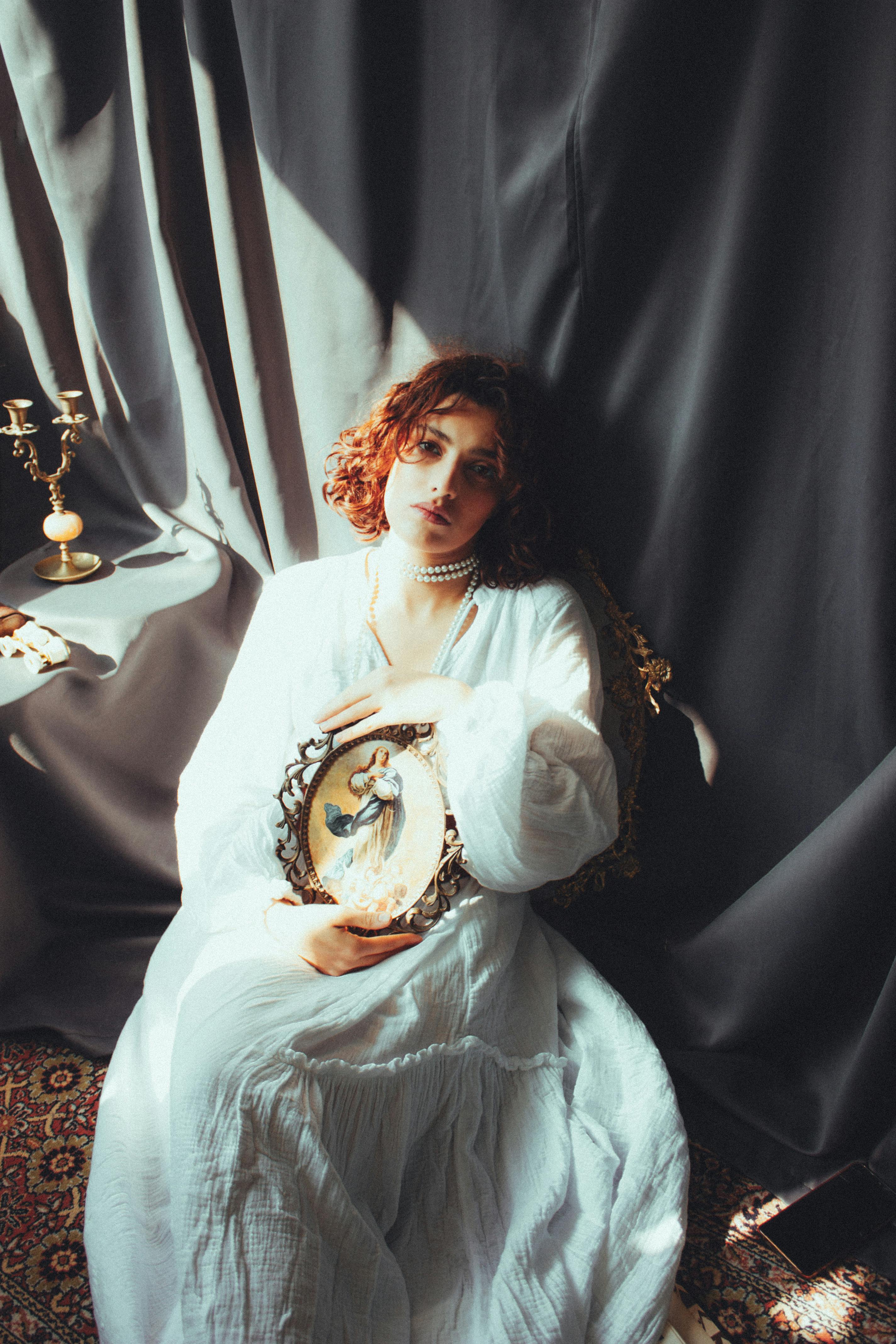 Elegant woman in white dress with picture frame in vintage setting.