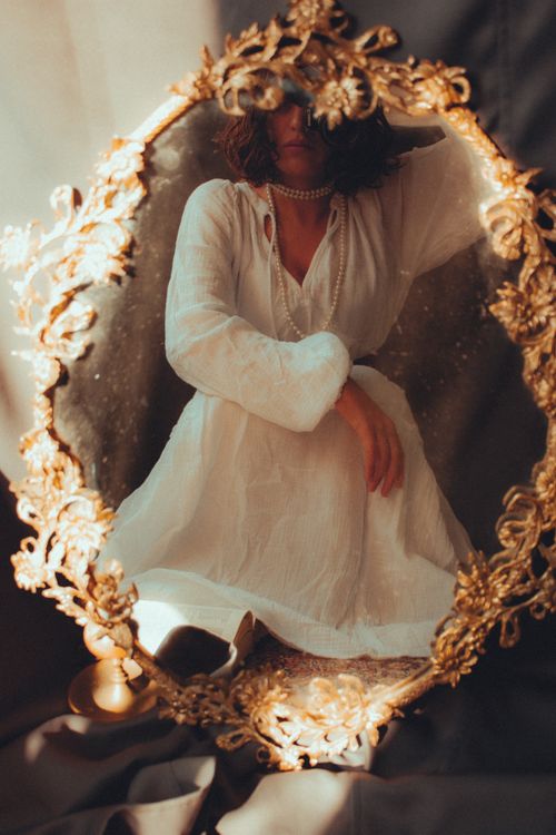 Free Elegant woman in white dress reflected in ornate golden mirror, soft lighting. Stock Photo