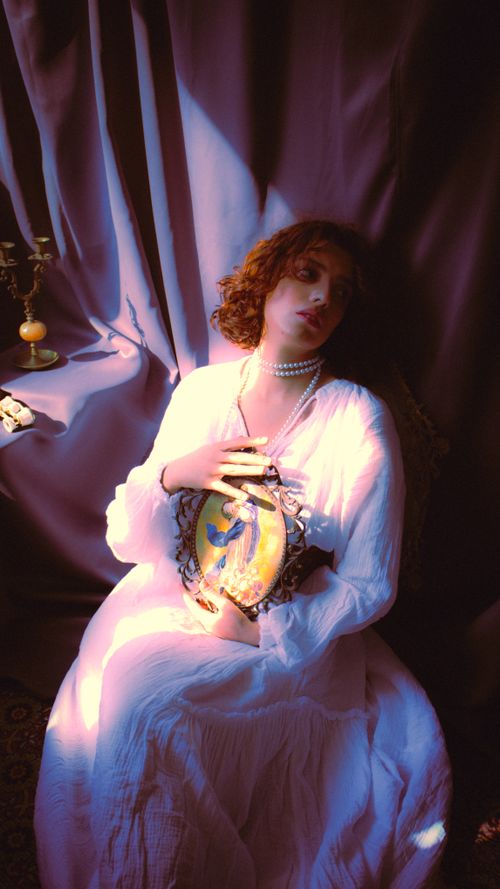 Free Elegant woman in vintage attire holding a framed artwork, bathed in warm, moody light. Stock Photo