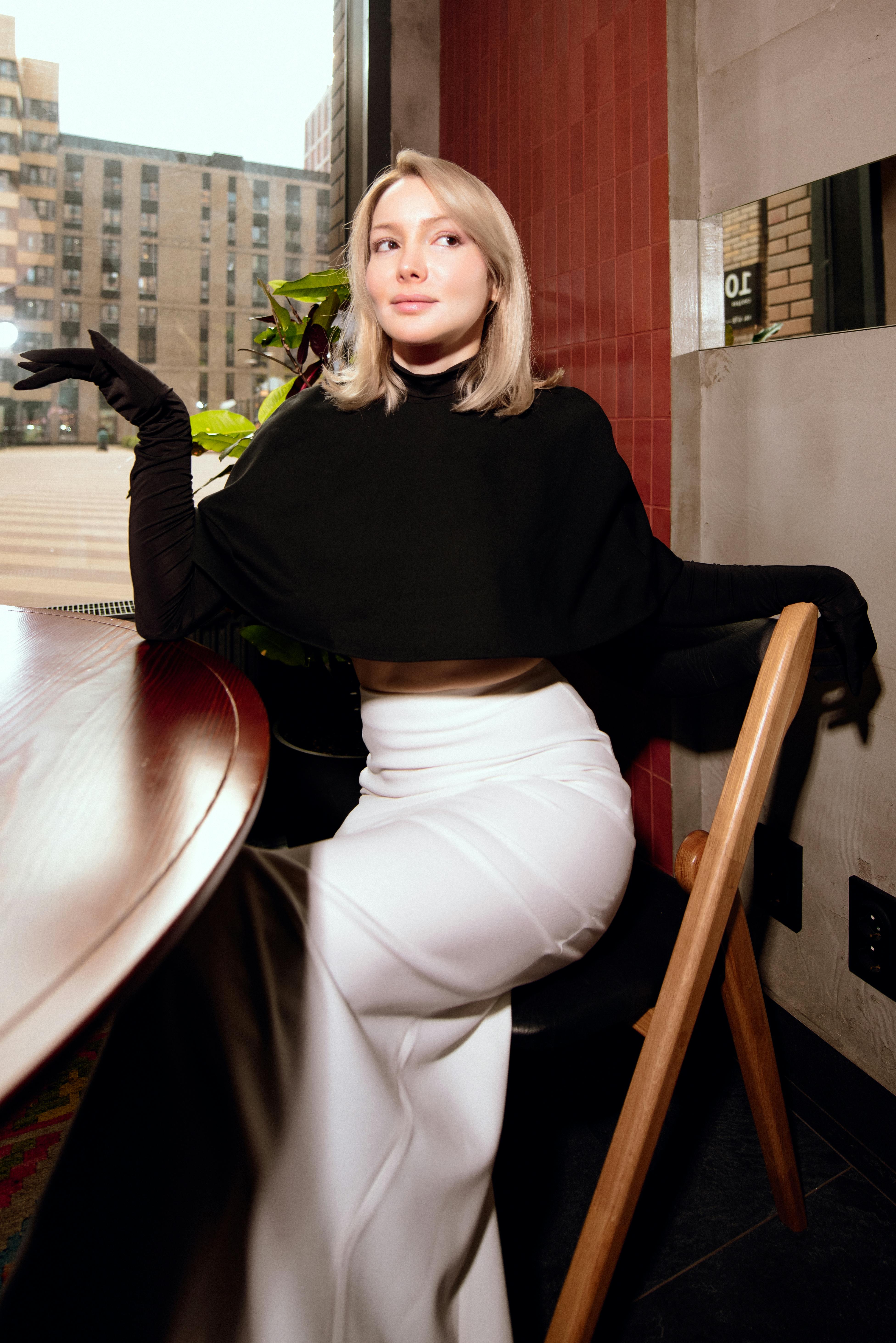 бесплатная Стильная женщина в черно-белом наряде позирует у окна в помещении. Стоковое фото