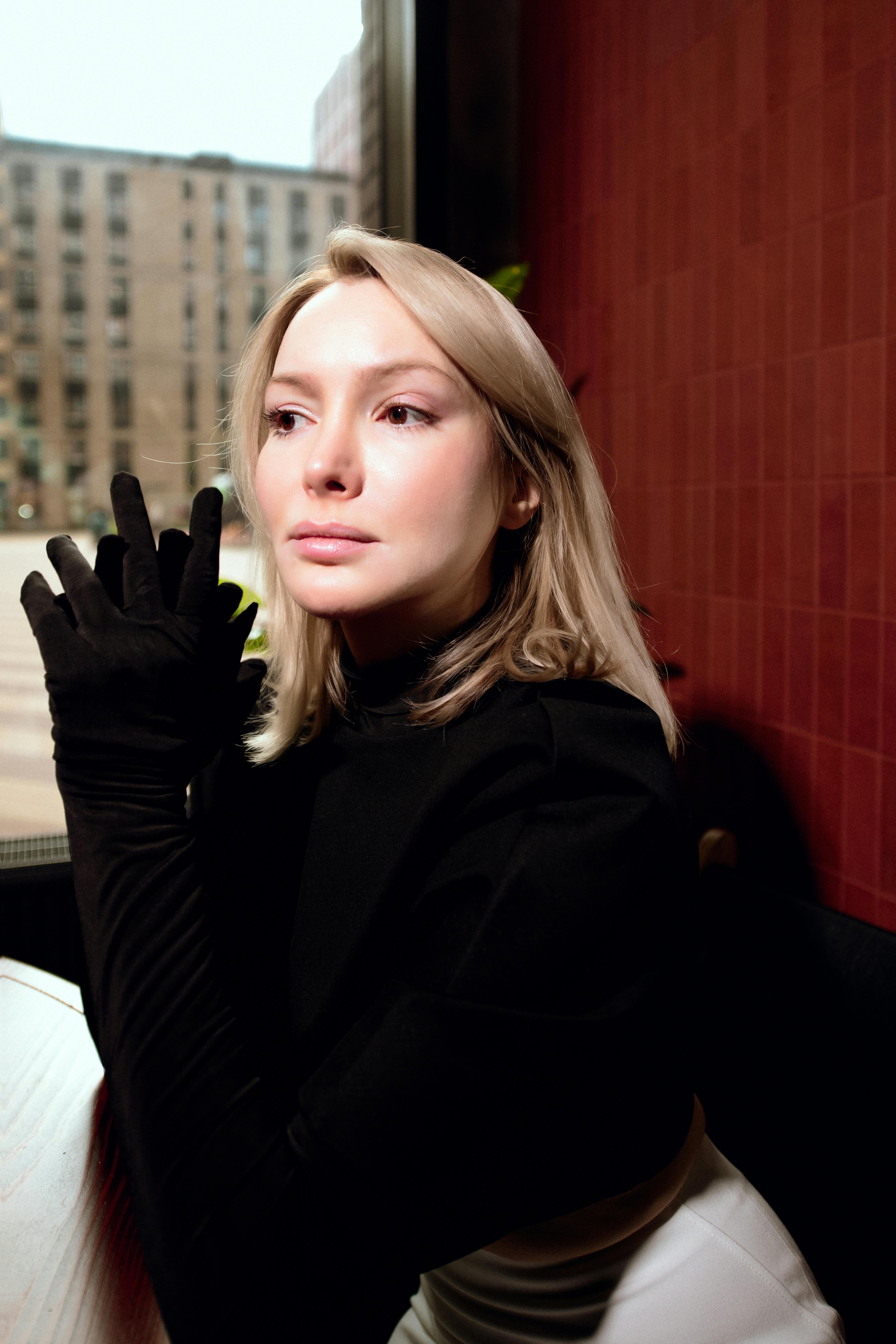 Kostnadsfria Sofistikerad kvinna med blont hår som bär svarta handskar i en modern kafémiljö. Stock foto