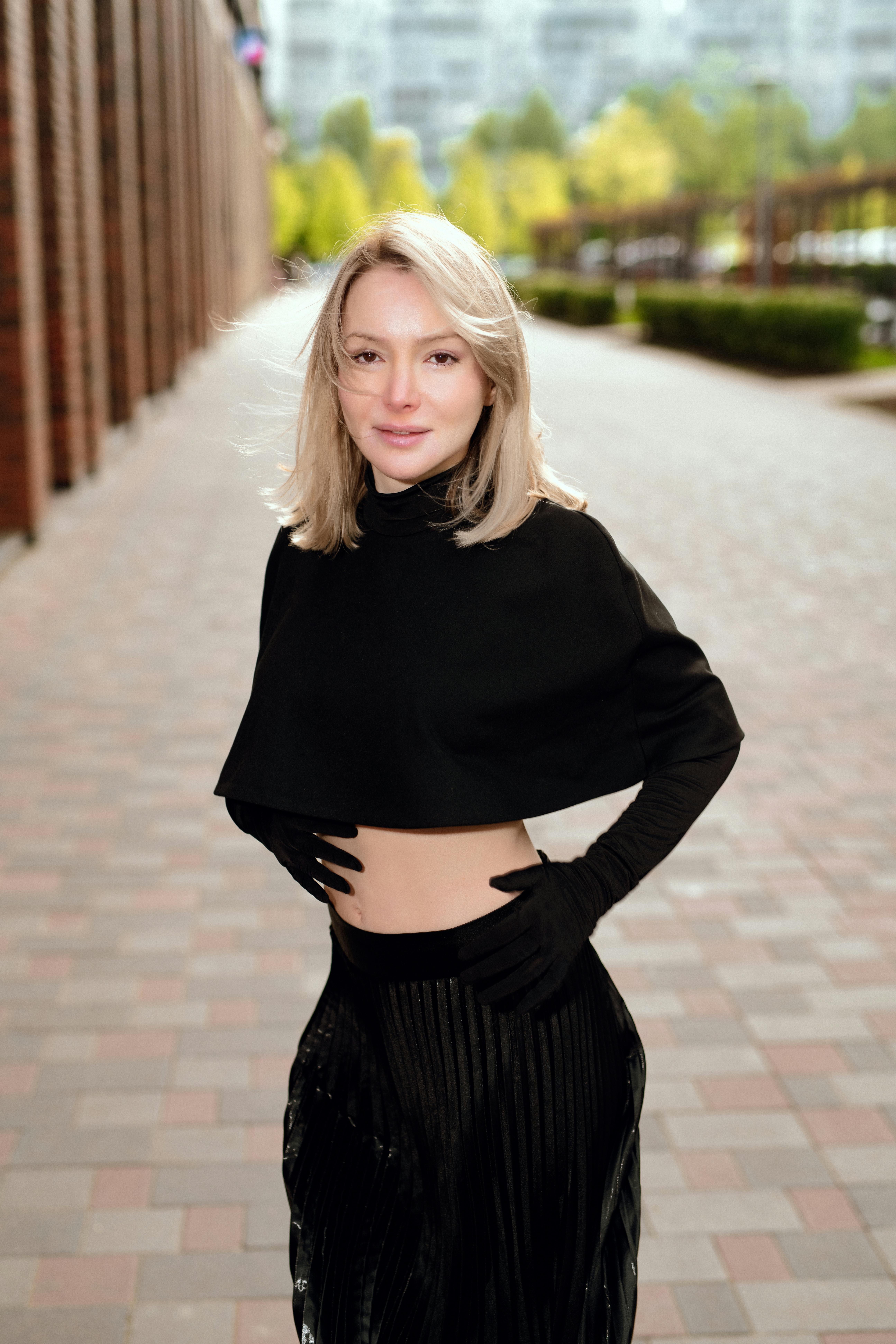 Gratis Una mujer elegante vestida de negro posa con confianza al aire libre en una pasarela pavimentada. Foto de stock