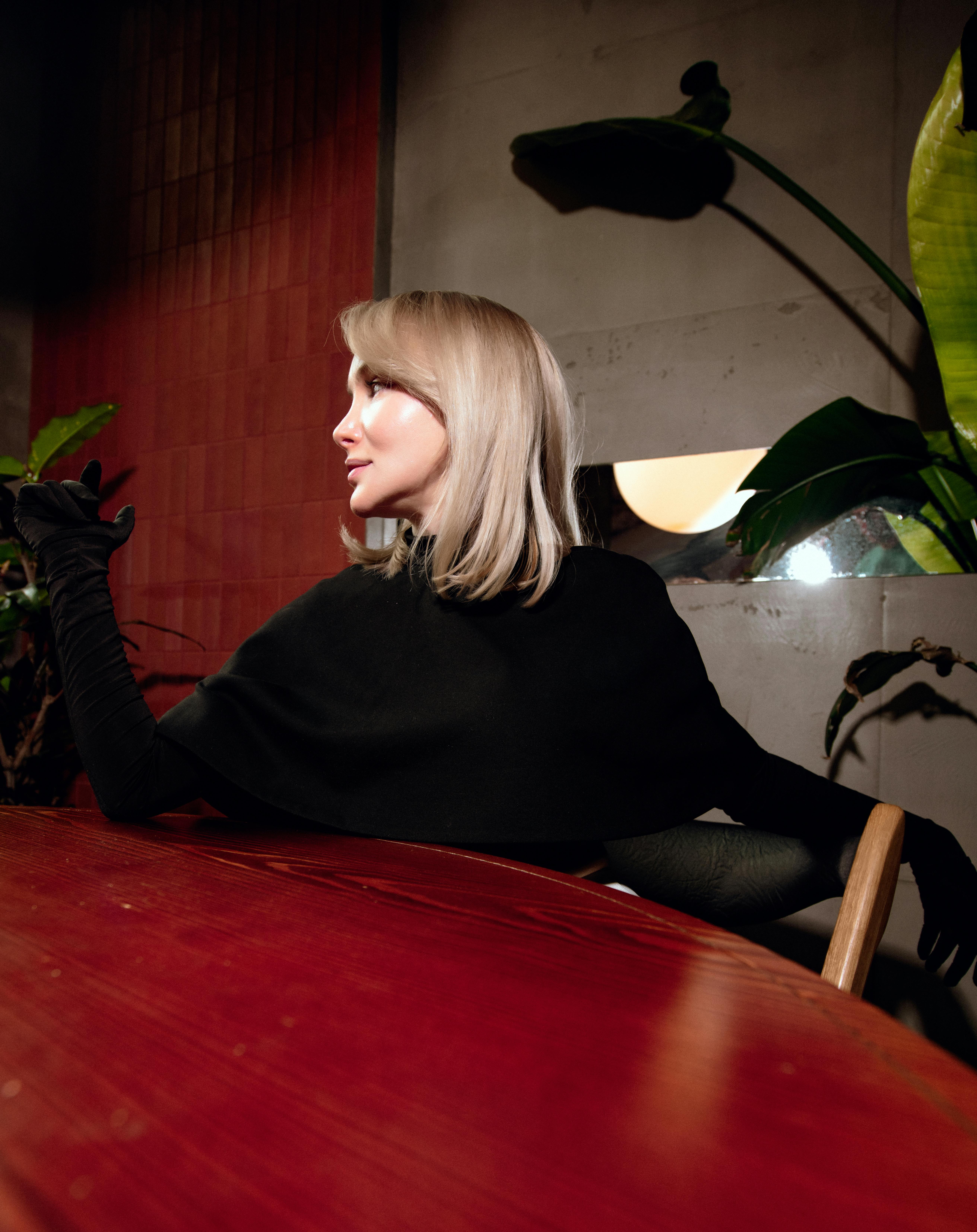 Kostnadsfria Elegant kvinna i aftonkläder sitter inomhus med växter och konstnärlig belysning. Glamorös atmosfär. Stock foto