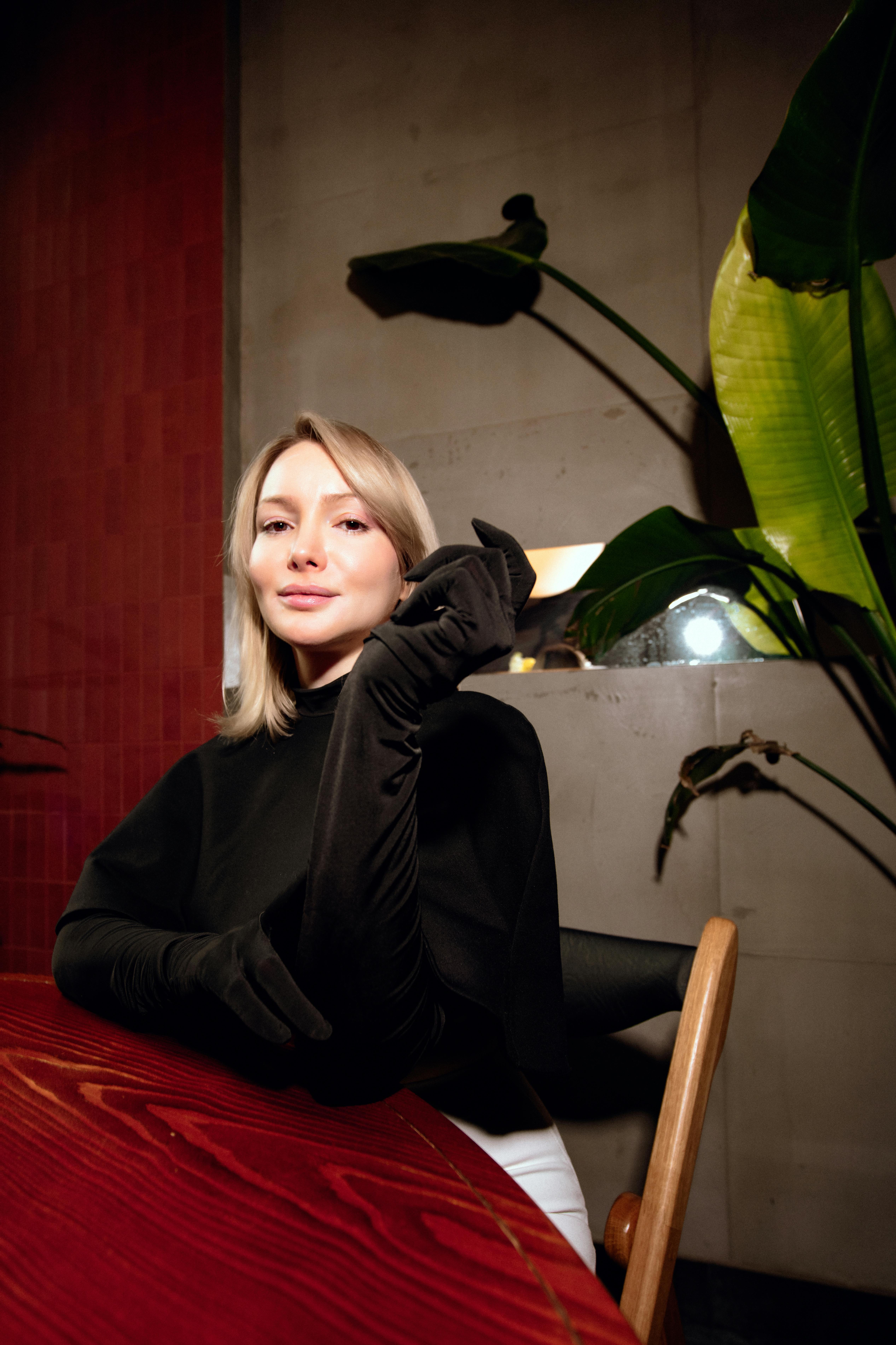 Zadarmo Štýlová žena sediaca v interiéri v dlhých čiernych rukaviciach, vyžarujúca eleganciu a sofistikovanosť. Fotka z fotobanky