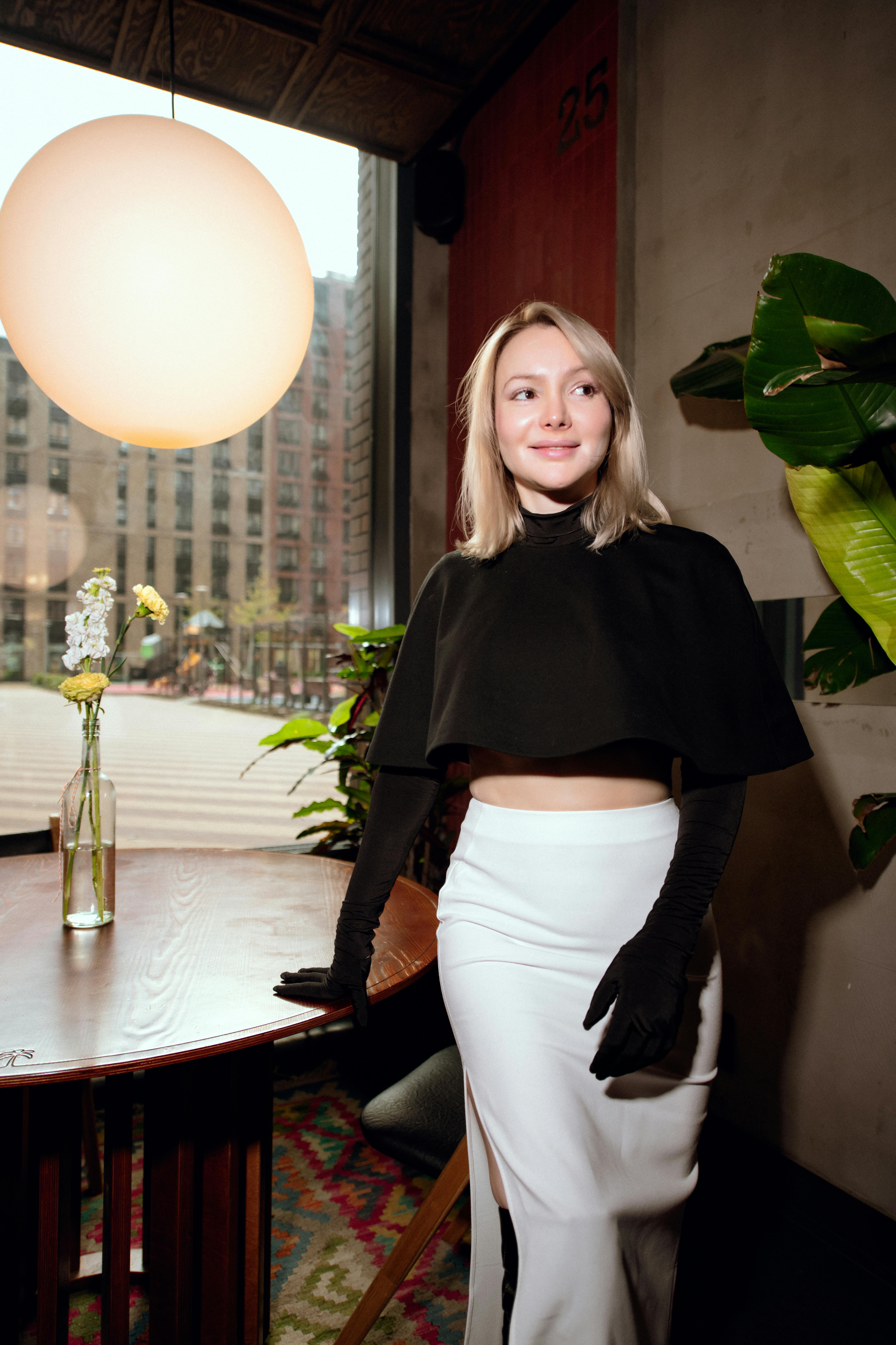 бесплатная Элегантная женщина стоит в помещении с современным декором и видом на городской пейзаж. Стоковое фото