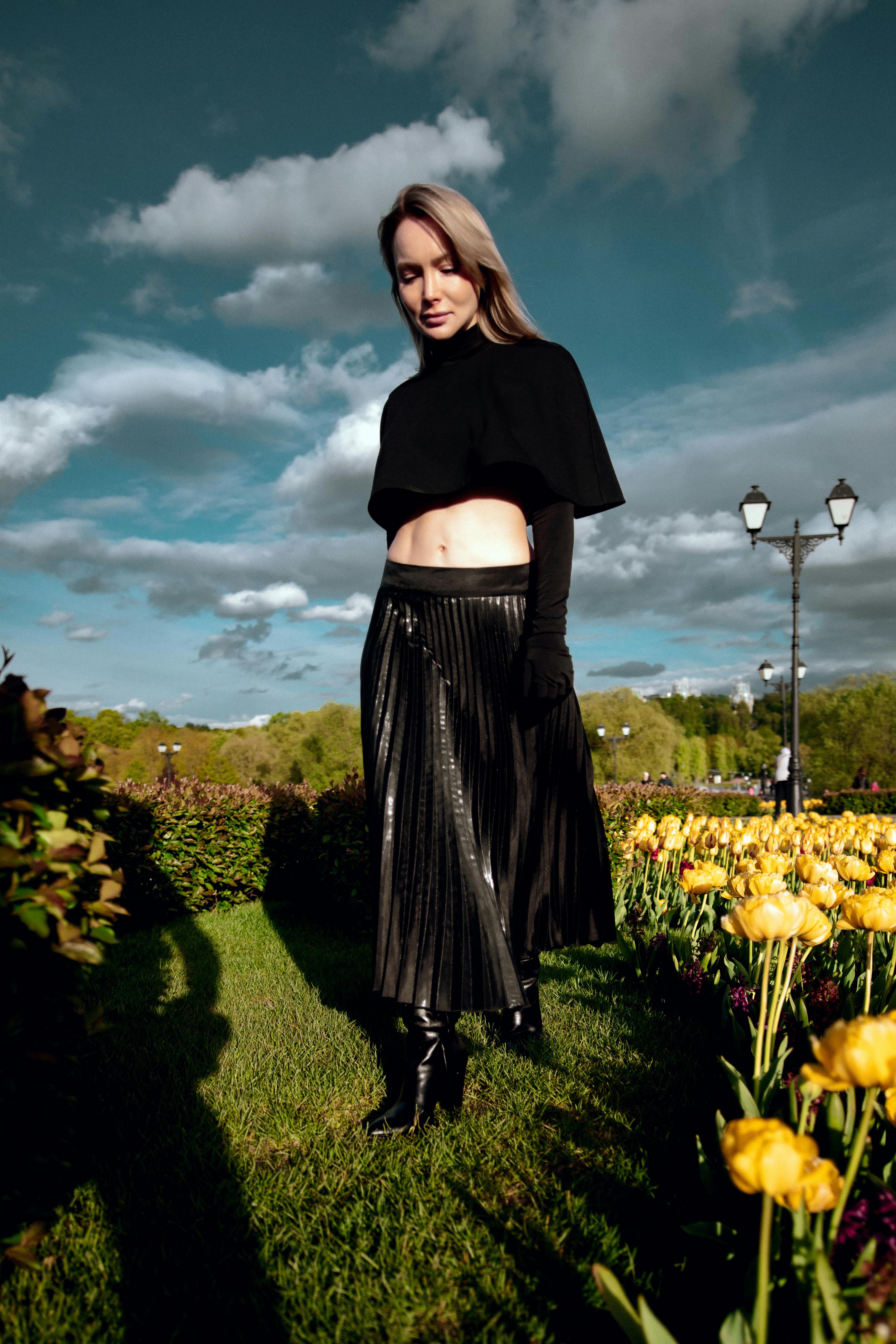 bezplatná Stylová žena v černém oblečení pózuje mezi zářivými květinami v zahradě. Základová fotografie