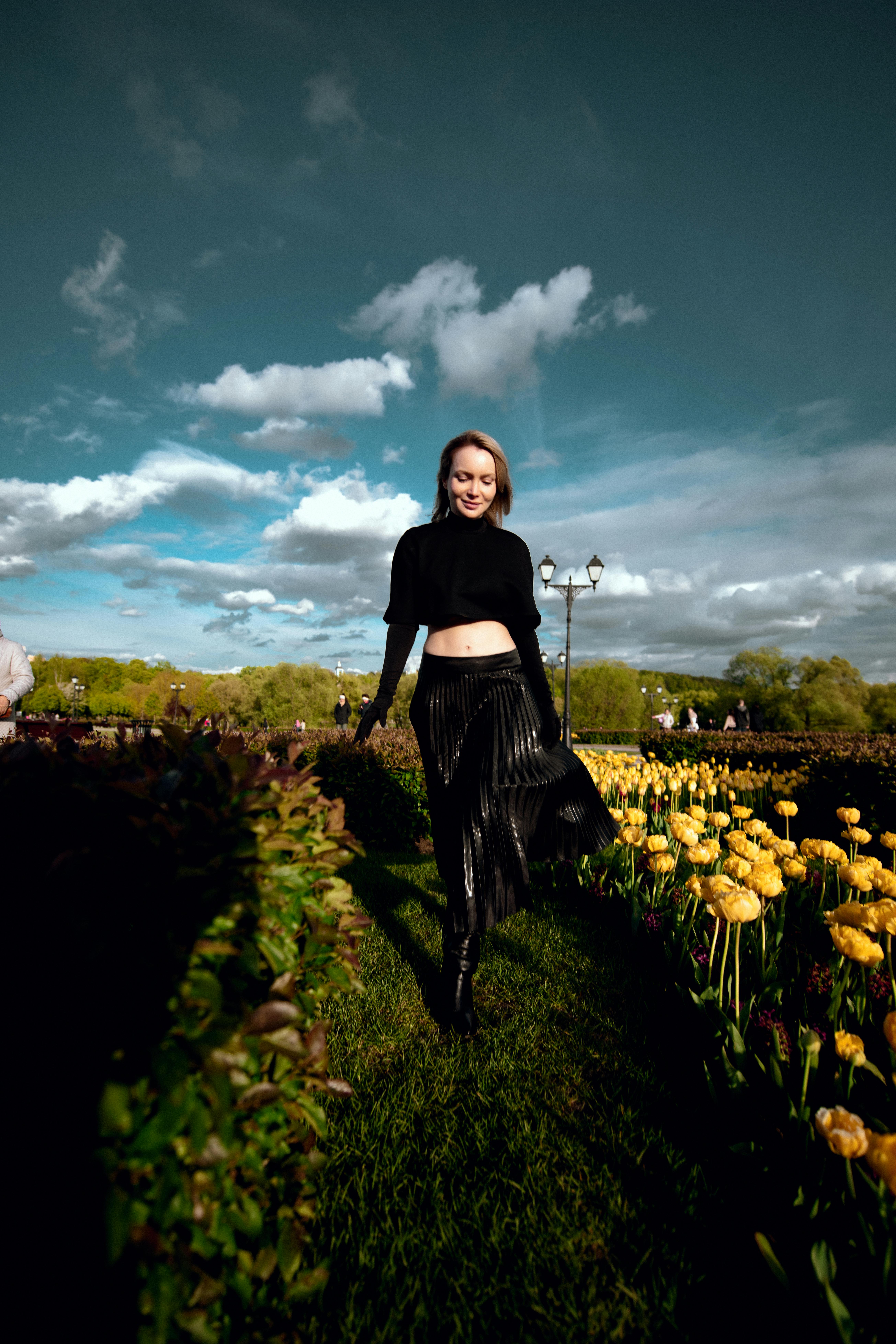 Gratis En ung kvinne går gledesfylt gjennom en frodig hage med gule tulipaner under en klar himmel. Arkivbilde