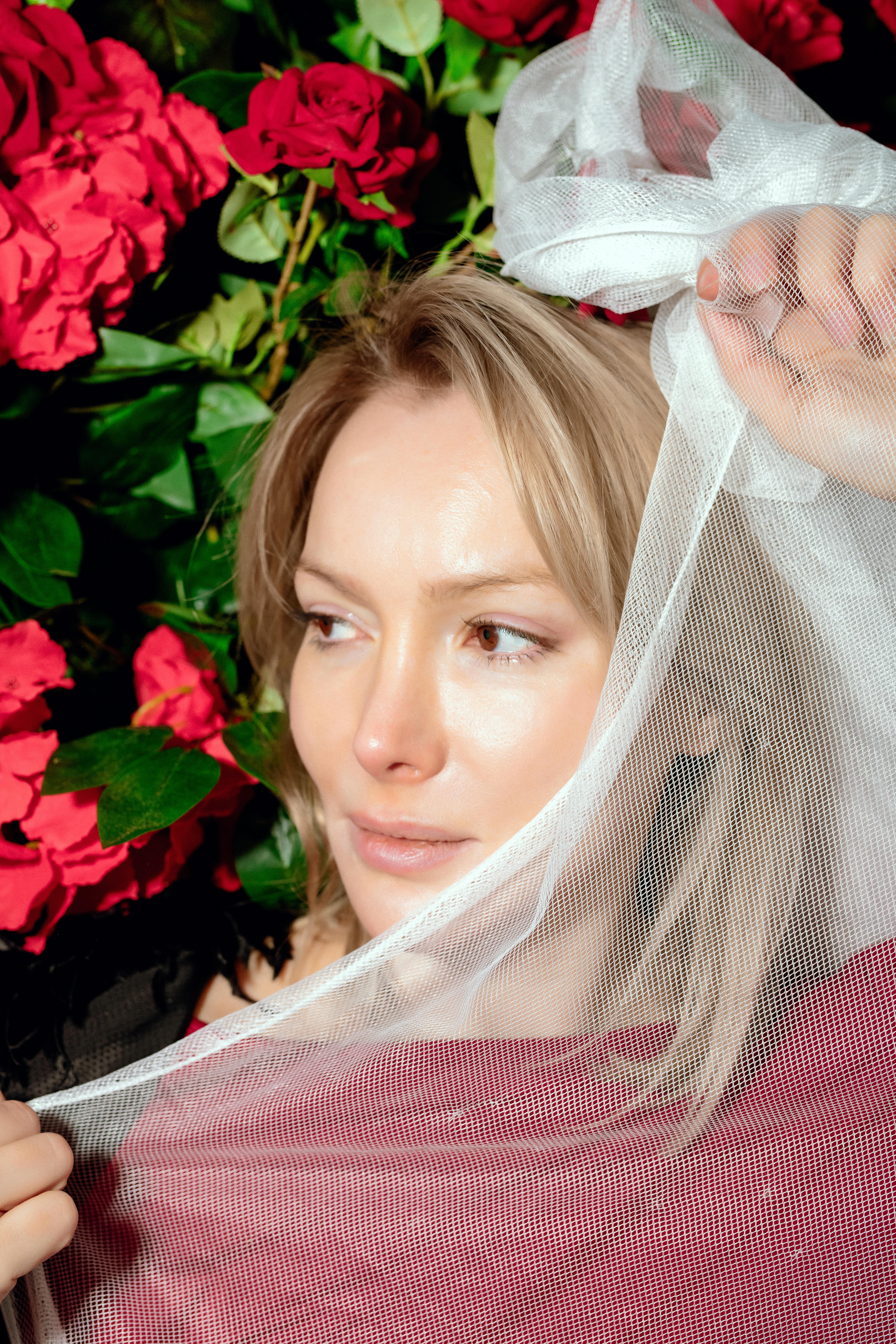 Bezpłatne Artystyczny portret kobiety pod przezroczystą tkaniną z jaskrawoczerwonymi różami. Zdjęcie z galerii