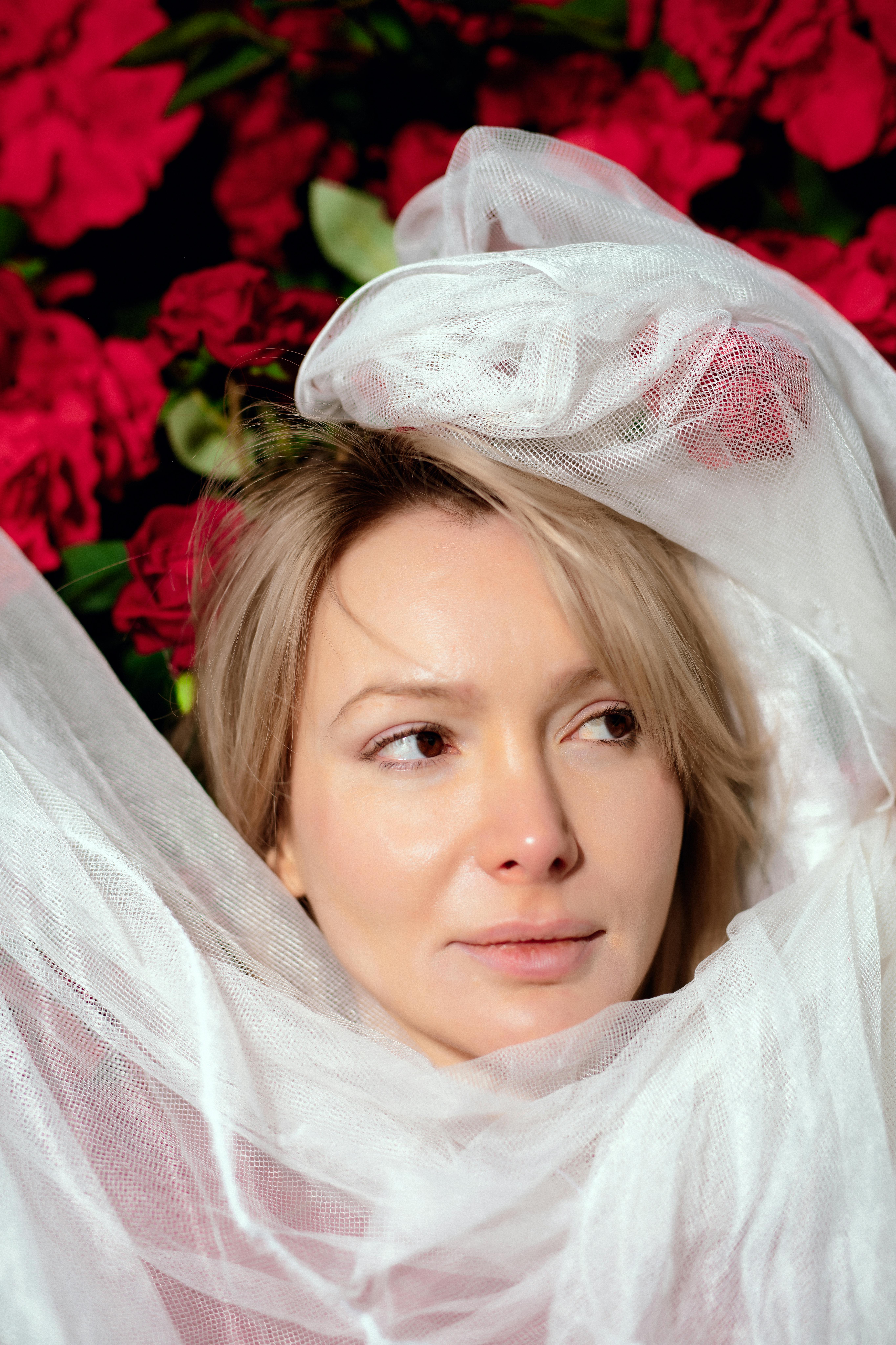 gratis Portret van een vrouw gewikkeld in witte stof met felrode bloemen op de achtergrond. Stockfoto